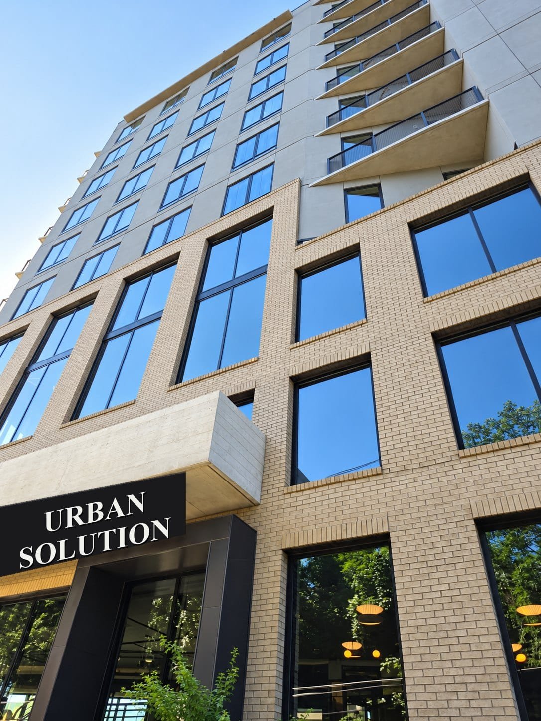 Looking up at a modern brick and concrete building with rows of black-framed aluminium windows and an Urban Solution sign